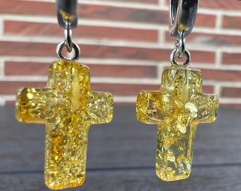 May include: A pair of silver hoop earrings with a yellow cross charm. The cross is made of clear resin with gold flecks.