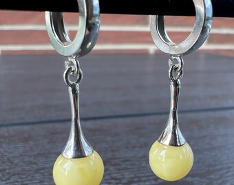 May include: A pair of silver hoop earrings with a dangling yellow amber drop on each earring.
