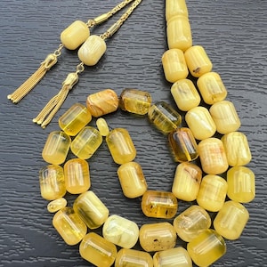 Peut inclure: Un chapelet avec un pompon doré et une chaîne de perles jaunes et ambrées. Les perles cylindriques varient en transparence, certaines étant opaques et d'autres translucides.