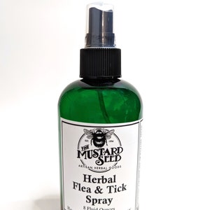 May include: A green glass bottle with a black spray nozzle and a white label. The label reads "The Mustard Seed Artisan Herbal Goods Herbal Flea & Tick Spray 8 Fluid Ounces Handmade in Little Falls, NY".