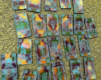 Puede incluir: Un conjunto de cartas de tarot con contornos turquesa y fondos coloridos y abstractos. Cada carta presenta ilustraciones únicas y títulos como "La Luna", "El Diablo" y "La Muerte". Las cartas están dispuestas sobre hierba verde.