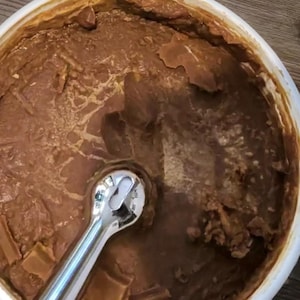 May include: A white bowl filled with a brown, textured food item. A shiny, silver wrench is partially submerged in the food. The food appears to have a thick, chunky consistency.