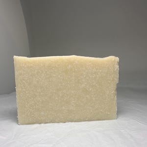 Può includere: Una saponetta rettangolare di sapone naturale di colore beige chiaro e con una texture leggermente granulosa.
