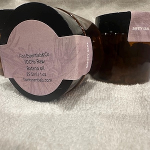 Puede incluir: Tres frascos de vidrio marr&oacute;n con tapas negras. Cada frasco tiene una etiqueta de color lila claro con el texto "Fiori Essentials&Co 100% Raw Batana oil 29,5 ml / 1 oz fioriessentials.com". Las etiquetas tambi&eacute;n dicen "SAFETY SEAL".