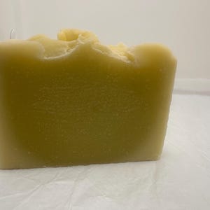 May include: A large, rectangular bar of handmade soap with a light green color and a rough, textured surface.