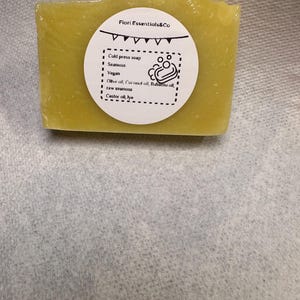 May include: A rectangular, yellow-green cold press soap bar wrapped in clear plastic. A white circular label displays the text "Fiori Essentials&Co" and lists ingredients including seamoss, olive oil, and castor oil. The soap is vegan.