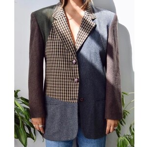 May include: A multi-patterned blazer featuring a brown and black gingham front panel, a grey herringbone panel, and solid dark brown sleeves. The garment includes a notched lapel, three front buttons, and two side pockets, constructed with a mix of textures.
