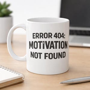 May include: White ceramic mug with the text "ERROR 404: MOTIVATION NOT FOUND" in black. The mug has a curved handle and is sitting on a wooden surface. A pen and notebook are also visible.