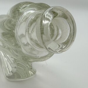 May include: Clear glass decorative bottle with a bulbous body and a flared opening. The glass has a swirling, textured pattern throughout. The bottle has a unique, artistic design, suitable for display or as a decorative piece.