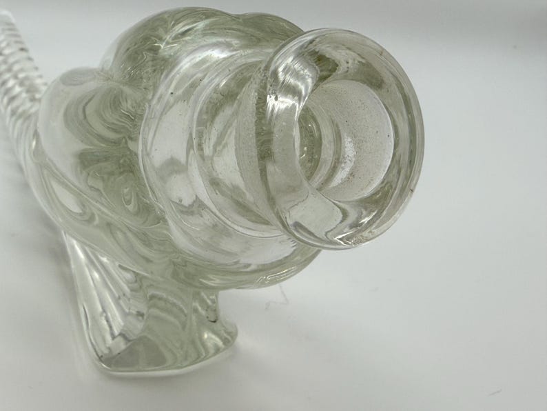 May include: Clear glass decorative bottle with a bulbous body and a flared opening. The glass has a swirling, textured pattern throughout. The bottle has a unique, artistic design, suitable for display or as a decorative piece.