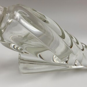 May include: Clear glass perfume bottle with a spiral design. The bottle has a long, twisted body and a small, rounded base. The stopper is visible at the top. The bottle is made of clear glass and is likely vintage.