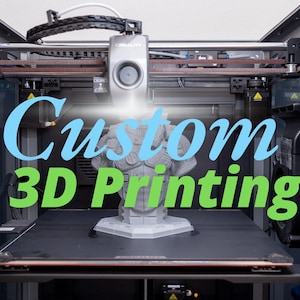 May include: A 3D printer with a gray plastic bust being printed. The printer has a black and silver frame and a brown belt. The text "Custom 3D Printing" is displayed on the front of the printer.