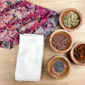 May include: A white fabric square, a patterned fabric square, and four wooden bowls filled with different natural materials. The bowls contain dried herbs, wood chips, spices, and black seeds.