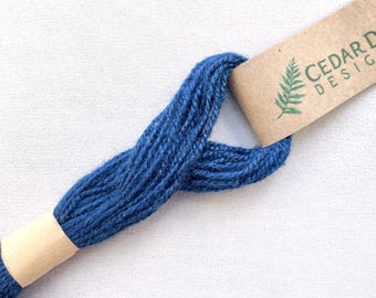 Puede incluir: Un ovillo de hilo de bordar azul oscuro con una etiqueta de papel marrón que dice "Cedar Design".