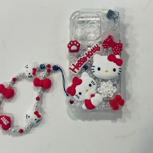 Puede incluir: Una funda transparente para tel&eacute;fono con un dise&ntilde;o de Hello Kitty. La funda est&aacute; decorada con pedrer&iacute;a, lazos y personajes de Hello Kitty. Se incluye una correa para tel&eacute;fono de cuentas blancas y rojas con abalorios de Hello Kitty.