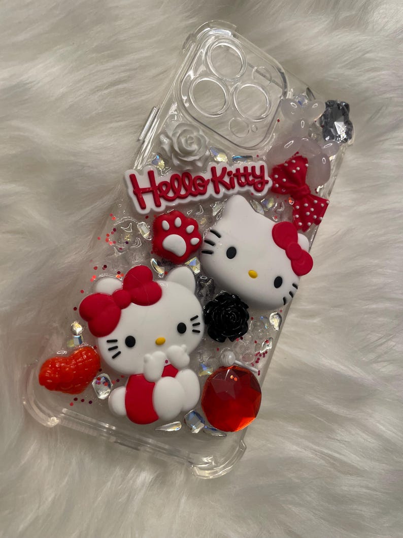 May include: Clear phone case with a red, white, and black Hello Kitty design. The case has glitter and rhinestones.