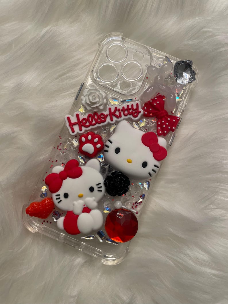 May include: Clear phone case with Hello Kitty characters, red bows, glitter, and rhinestones.