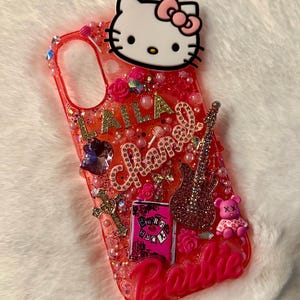 May include: A pink and red phone case featuring a Hello Kitty character, glitter, and the words "LALA Chanel Barbie" on it.