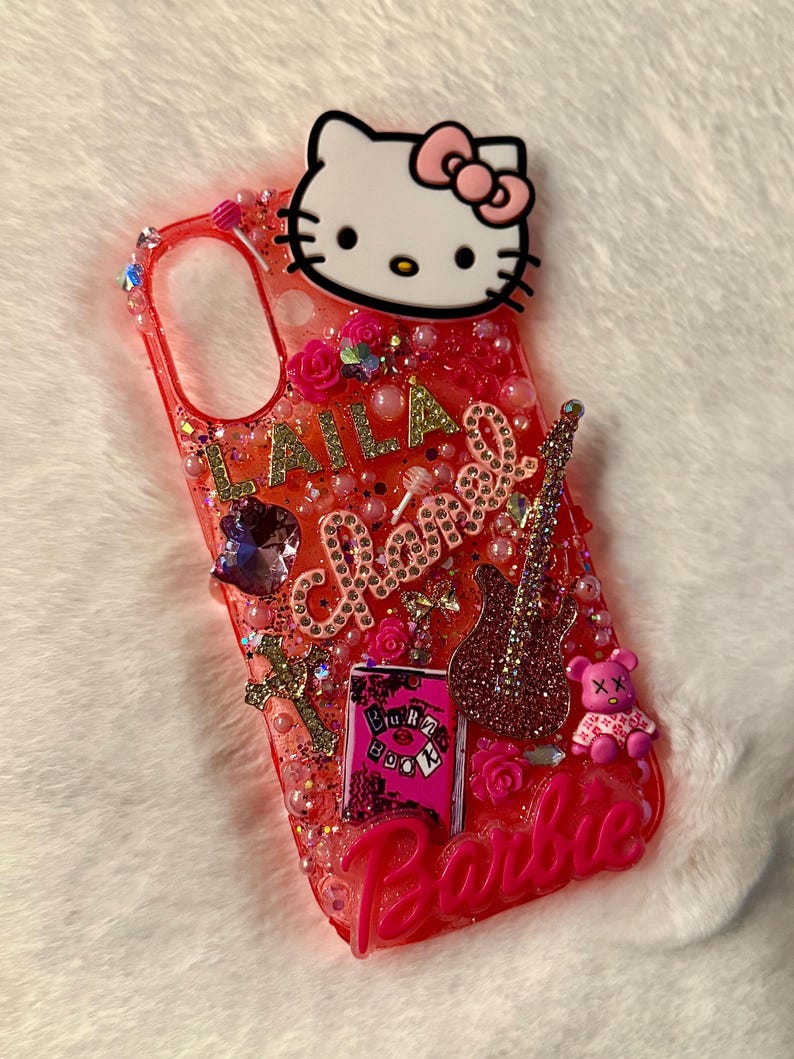 May include: A pink and red phone case featuring a Hello Kitty character, glitter, and the words "LALA Chanel Barbie" on it.