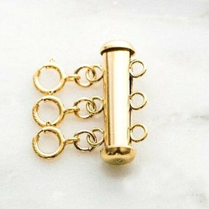 May include: Gold-toned metal four-strand connector for jewelry making. The connector has a cylindrical shape with four loops on each end.