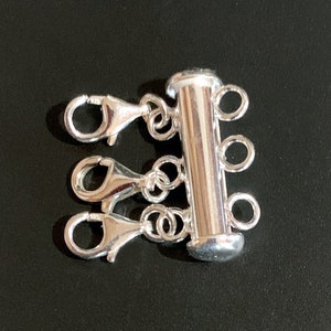 May include: Silver-toned multi-strand connector with three lobster claw clasps. The connector is cylindrical and has four loops for attaching strands of jewelry.