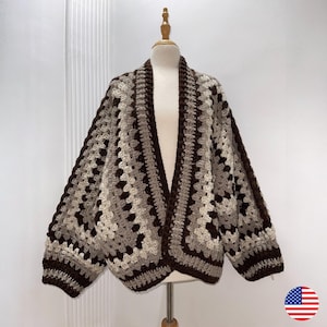 Può includere: Cardigan all'uncinetto fatto a mano, con motivo a granny square. La combinazione di colori include tonalità di marrone, beige e grigio. Il cardigan è esposto su un manichino, mostrando la sua vestibilità ampia e il design strutturato. Un capo comodo ed elegante.