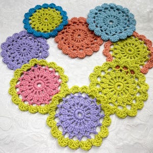 May include: A collection of handmade crochet coasters in various colors, including blue, green, pink, orange, and purple. Each coaster features a circular design with a scalloped edge, perfect for protecting surfaces from drink condensation.