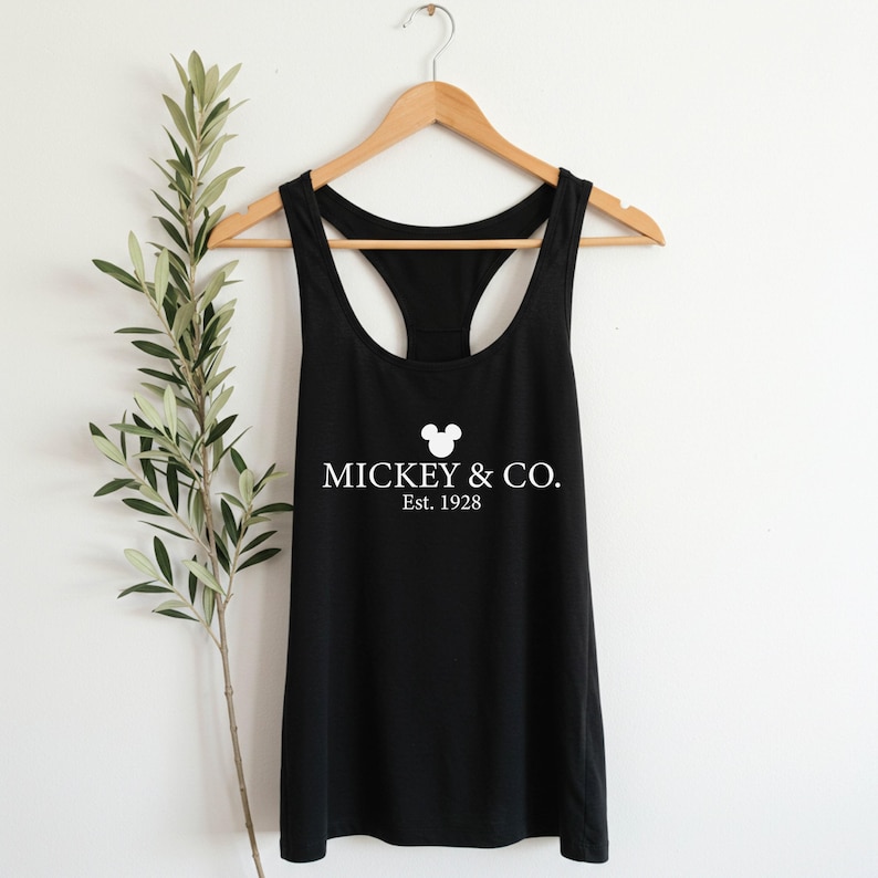 Puede incluir: Camiseta de tirantes negra con una cabeza de Mickey Mouse blanca y el texto "MICKEY & CO. Est. 1928"
