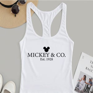Puede incluir: Camiseta blanca de tirantes con una cabeza de Mickey Mouse negra y el texto "Mickey & Co. Est. 1928"