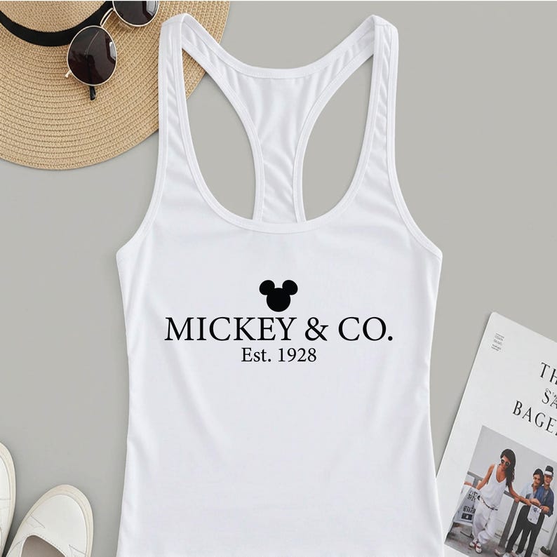 Puede incluir: Camiseta blanca de tirantes con una cabeza de Mickey Mouse negra y el texto "Mickey & Co. Est. 1928"