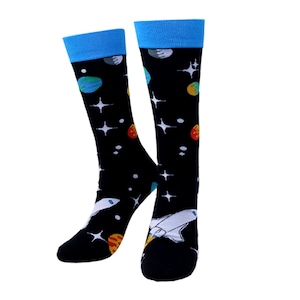 May include: A pair of black socks with a space-themed design. The socks feature a blue cuff and a pattern of planets, stars, and a white rocket ship. The planets are in shades of blue, yellow, and red.