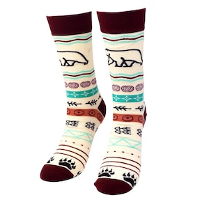 May include: A pair of cream-colored socks with a burgundy cuff, heel, and toe. The socks feature a repeating pattern of a bear silhouette, tribal designs, and bear paw prints in black, teal, and brown. The socks are designed for adults.