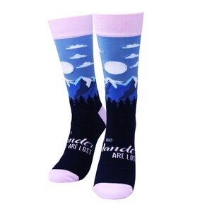 May include: A pair of knee-high socks with a mountain and sky design. The socks feature a blue sky with white clouds, blue mountains, and a forest silhouette. The text "When wander are lost" is printed on the socks. The socks have pink cuffs and toes.
