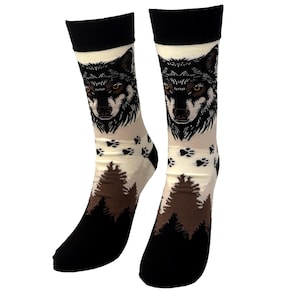 May include: Crew socks with a wolf face design. The socks have a black cuff, heel, and toe, with a cream-coloured body. The design includes paw prints and a forest scene in shades of brown. The socks are designed to be worn on the feet.