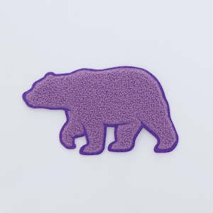 Op de afbeelding: Een paarse berenpatch met een getextureerde, fuzzy uitstraling. De beer loopt naar rechts, met een donkerdere paarse omtrek. De patch is waarschijnlijk voor kleding of accessoires.