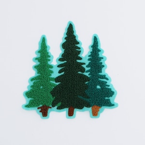 Puede incluir: Parche bordado con tres árboles de hoja perenne estilizados en tonos verdes y turquesas. Los árboles tienen un aspecto texturizado y están delineados con un borde turquesa. Los troncos de los árboles son marrones, sobre un fondo blanco.