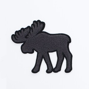 May include: A dark gray moose patch with a black outline. The patch has a textured, fuzzy appearance and is set against a white background. The moose is depicted in a side profile, showcasing its antlers and body.