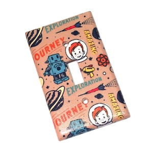 May include: A light pink light switch cover with a space-themed design. The cover features a robot, a rocket ship, planets, and the words "Journey", "Exploration", and "Amazing".