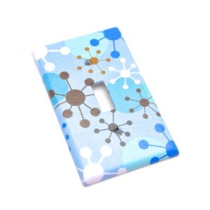 May include: A light blue light switch cover with a white, brown, and blue geometric pattern. The pattern features circles and starbursts.
