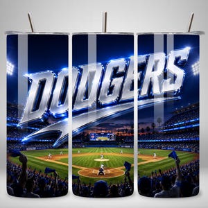 May include: A cylindrical tumbler with a metal straw featuring a graphic of a baseball stadium at night. The word DODGERS is printed in large, metallic, three-dimensional silver letters across the top. The scene shows a baseball game in progress.
