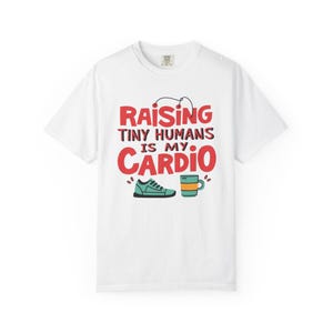Può includere: T-shirt bianco con la scritta "Raising Tiny Humans Is My Cardio" in rosso e nero. Il design include una scarpa da ginnastica verde e una tazza turchese con una striscia arancione. Una maglietta casual.
