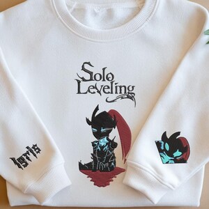 May include: White sweatshirt with a black and red illustration of a character from the Solo Leveling manga. The text "Solo Leveling" is printed in black above the character. The text "Igris" is embroidered on the left sleeve.