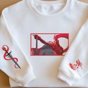 Puede incluir: Sudadera blanca con ilustraciones bordadas. El dise&ntilde;o presenta una ilustraci&oacute;n roja y gris de una figura sosteniendo una espada, enmarcada en rojo. Detalles bordados adicionales incluyen una espada con una cinta roja y una figura m&aacute;s peque&ntilde;a en la manga.