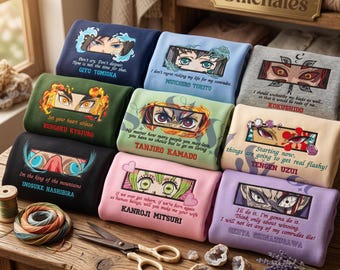 May include: A collection of folded sweatshirts featuring embroidered anime character eyes and quotes. Each garment displays a unique character name, including Giyu Tomioka, Rengoku Kyojuro, and Tanjiro Kamado, in various colors like navy, olive, and light blue.