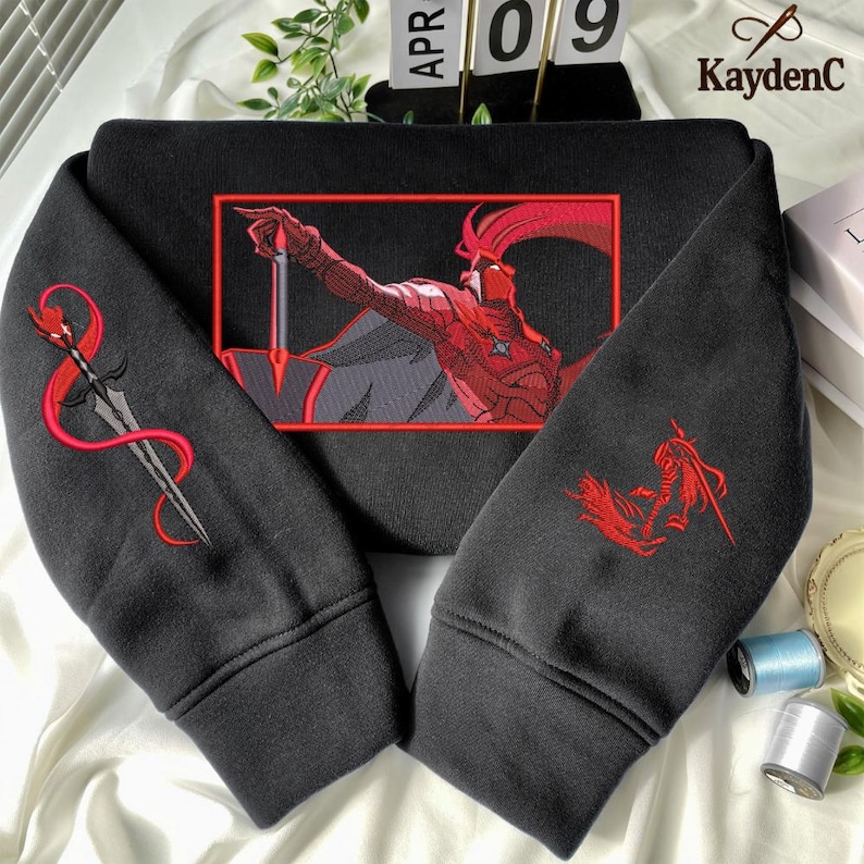 Puede incluir: Sudadera negra con bordados rojos. La parte delantera presenta un gr&aacute;fico rojo y negro de una figura sosteniendo una espada. La manga izquierda tiene un dise&ntilde;o de espada y la manga derecha un dise&ntilde;o de figura. La marca "KaydenC" es visible.