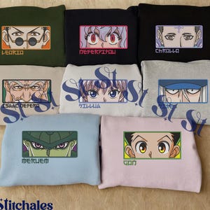 May include: A collection of sweatshirts in various colors, each featuring embroidered anime character eyes and names. The sweatshirts include designs with Leorio, Neferpitou, Chrollo, Isaac Netero, Killua, Meruem, and Gon. The brand name "Stitchales" is at the bottom.