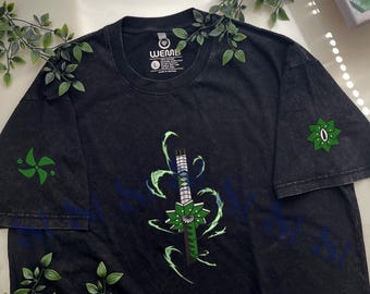 May include: A black acid-wash t-shirt featuring a central graphic of a sword with a green and silver hilt surrounded by light green energy swirls. The sleeves display green star-shaped emblems. The inner neck label reads WEMB and size L.