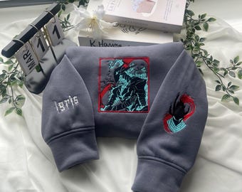 May include: A grey hoodie featuring a central square embroidery of a dark armoured figure with teal and red accents. The left sleeve displays the embroidered text Igris in white, while the right sleeve features a red and teal graphic emblem.
