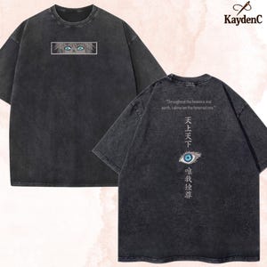 Può includere: Una t-shirt grigio antracite lavaggio acido con una grafica rettangolare di occhi anime sul davanti. Il retro mostra un occhio blu, caratteri giapponesi e il testo: Throughout the heavens and earth, I alone am the honored one.