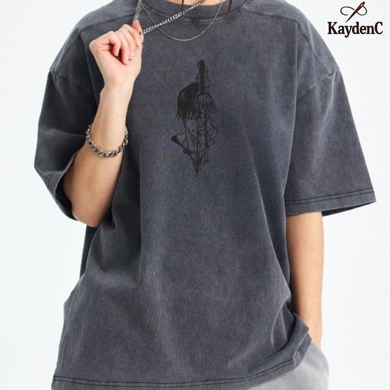 Puede incluir: Camiseta gris oscuro de gran tama&ntilde;o con un gr&aacute;fico negro de una persona con una espada. La camiseta tiene mangas cortas y cuello redondo. El logotipo de KaydenC est&aacute; en la esquina superior derecha.